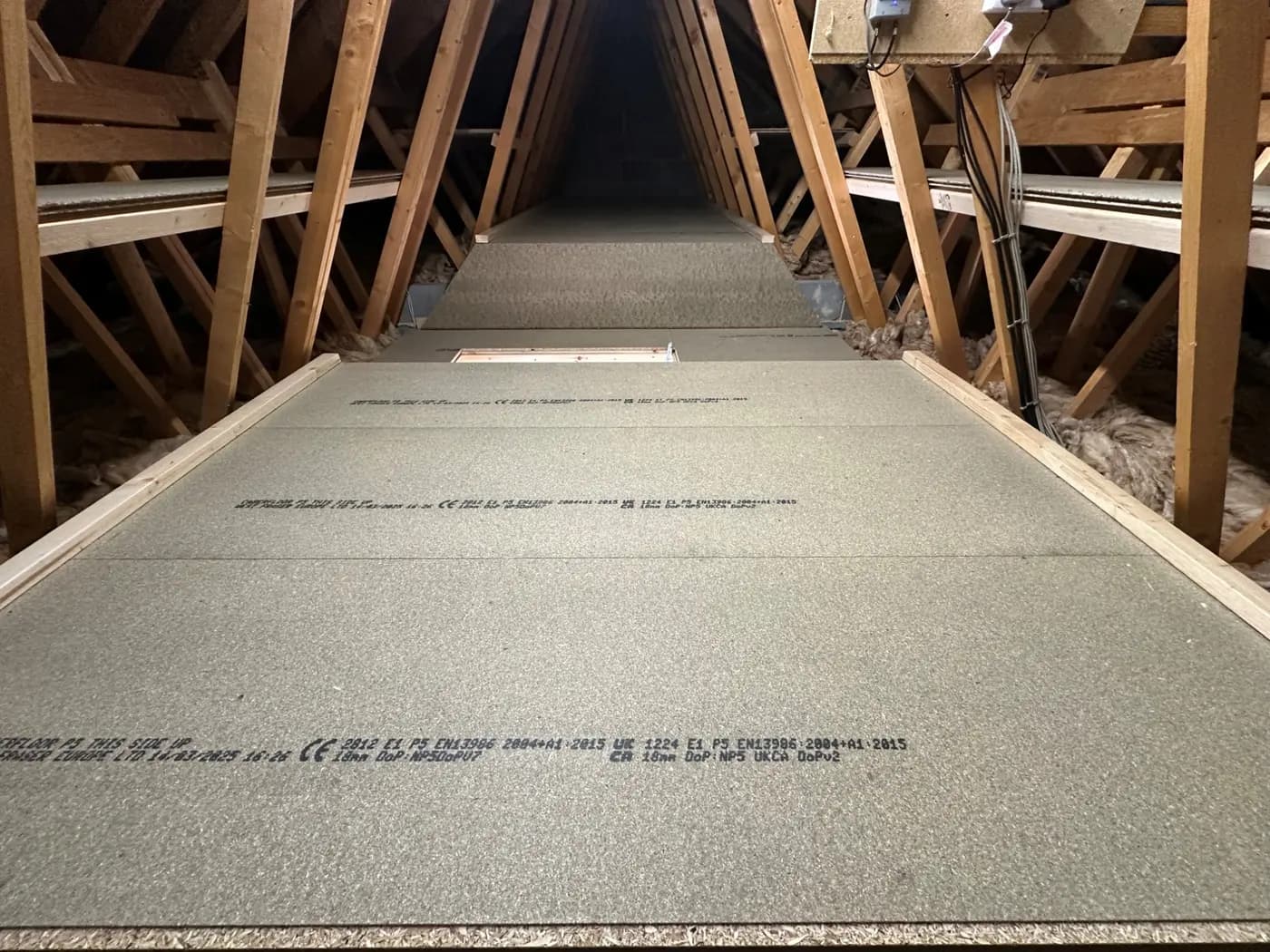 Raised loft boarding fitted across a roof space, with the timber trusses either side
