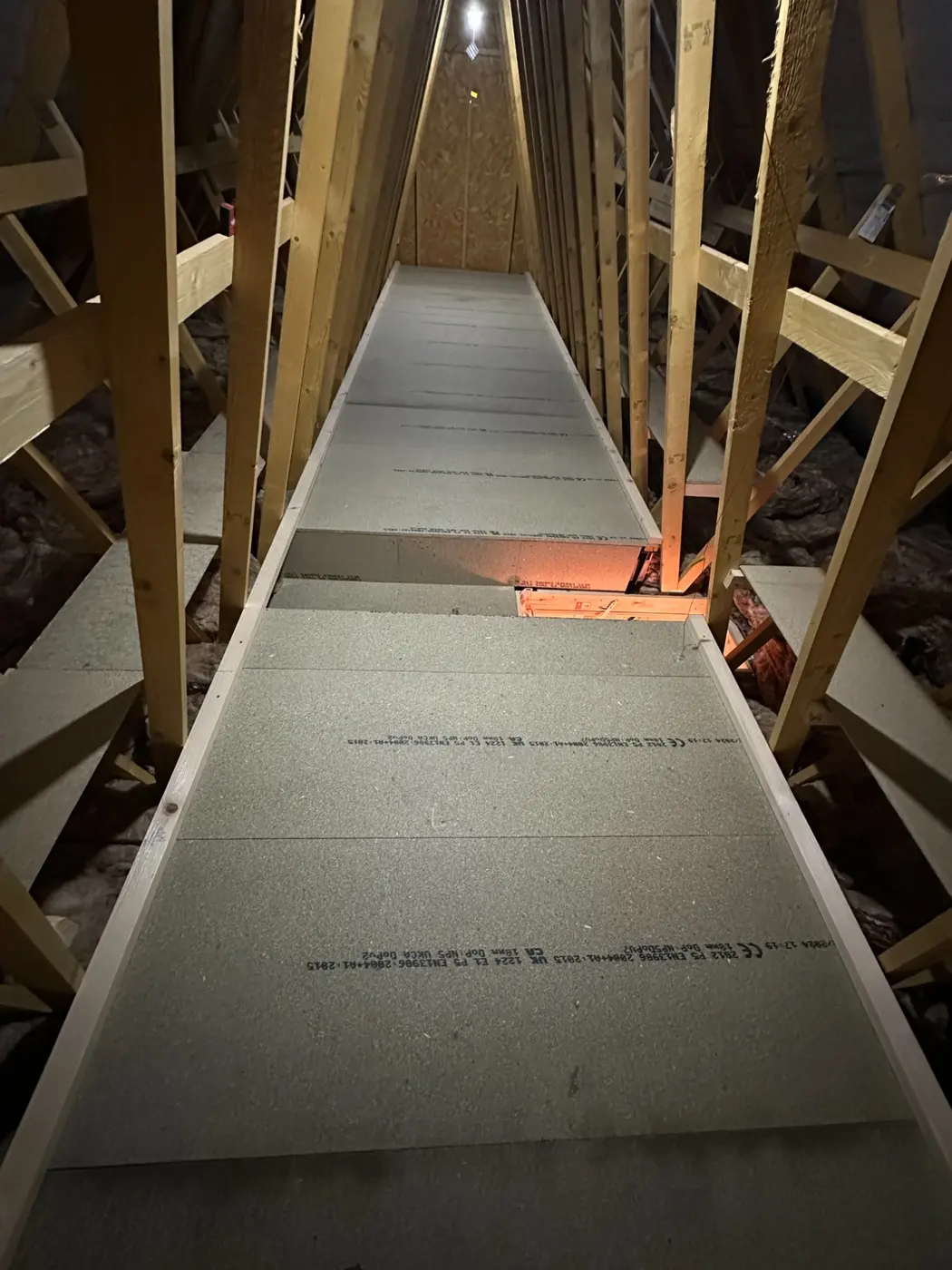 A long, newly boarded walkway running the length of a loft between the roof timbers